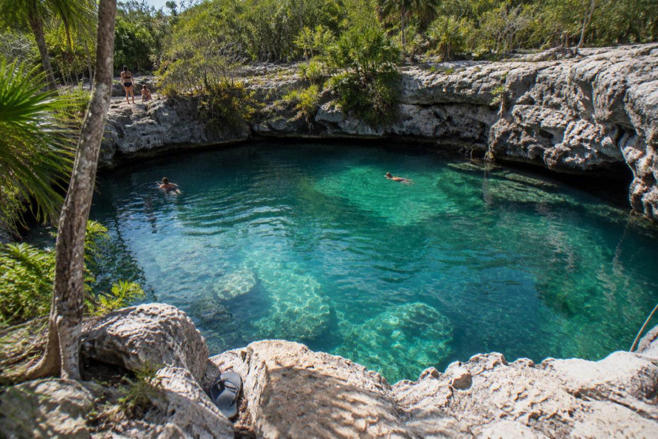 Clear turquoise water filling a rounded limestone sinkhole surrounded by jungle foliage and exposed rock