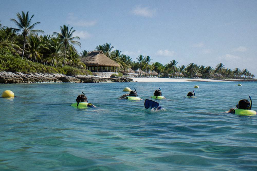 A small guided snorkel group floating together in calm bay water near buoys