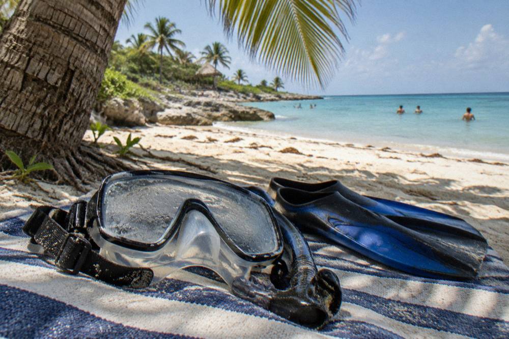 Snorkel mask and fins resting on a beach towel beside a shaded palm