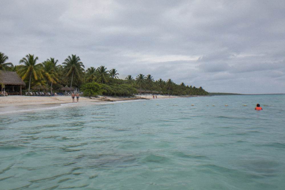 Wide view of a Caribbean bay with pale sand, palms and calm water beyond a protected swim area