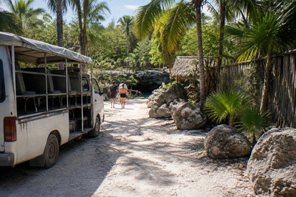 Open tour van parked on a jungle road beside limestone rock and palm trees