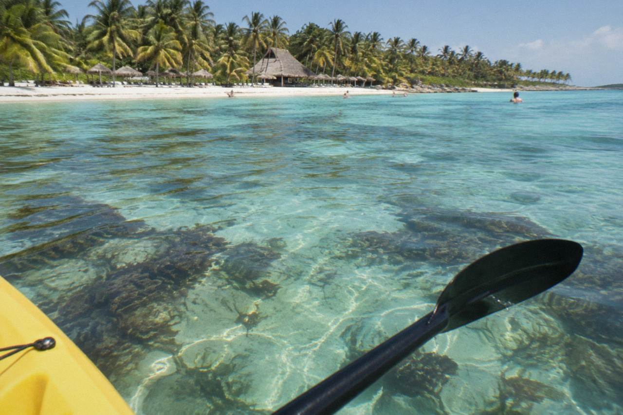 Calm turquoise water over a sandy bay floor with seagrass patches and distant palms