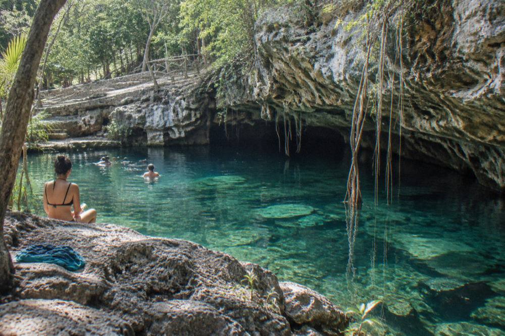Clear freshwater cenote surrounded by limestone rock and hanging tree roots