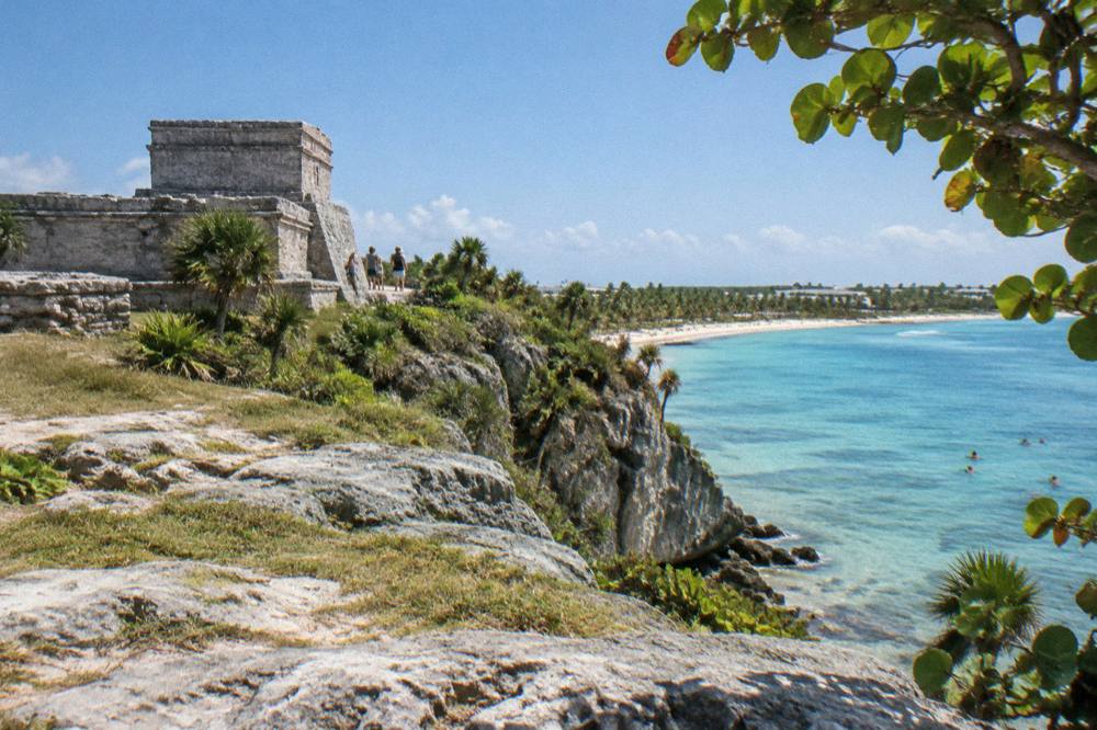 Stone ruins on a cliff above turquoise Caribbean water with trees framing the view