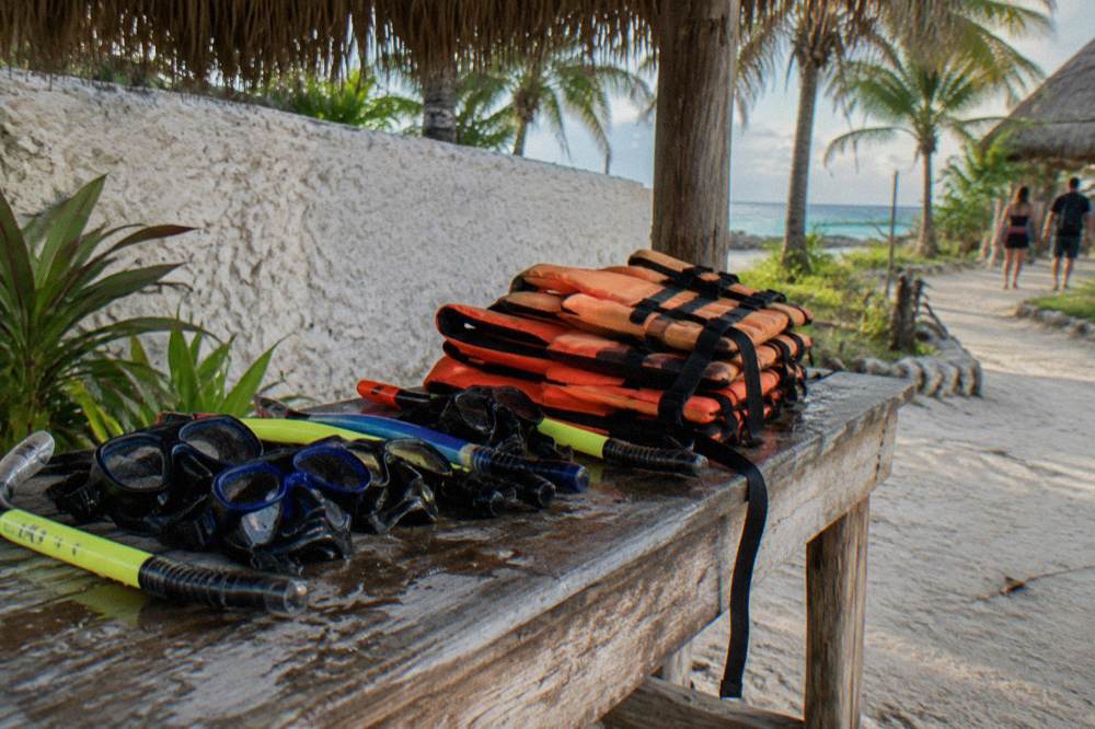 Snorkel gear and life vests laid out on a wooden bench beside a beach entrance