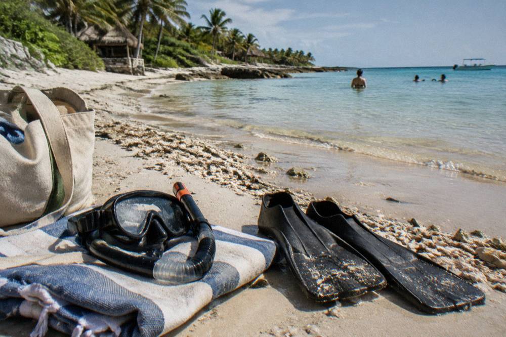 Snorkel mask and short fins resting on a towel beside a beach bag