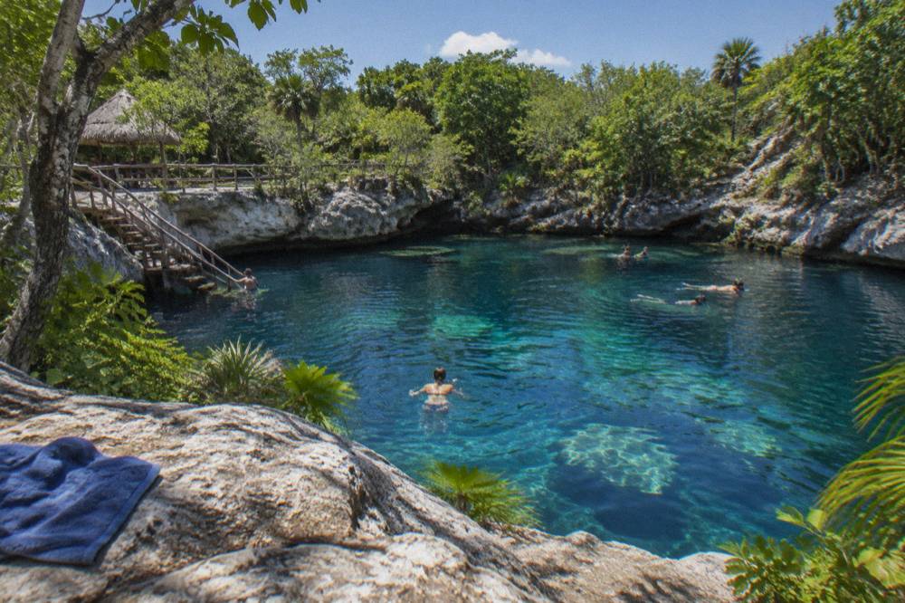 A freshwater cenote pool surrounded by rock and jungle vegetation