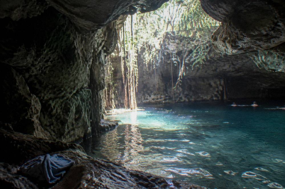 Sunlight falling through an opening in limestone rock onto pale blue cenote water