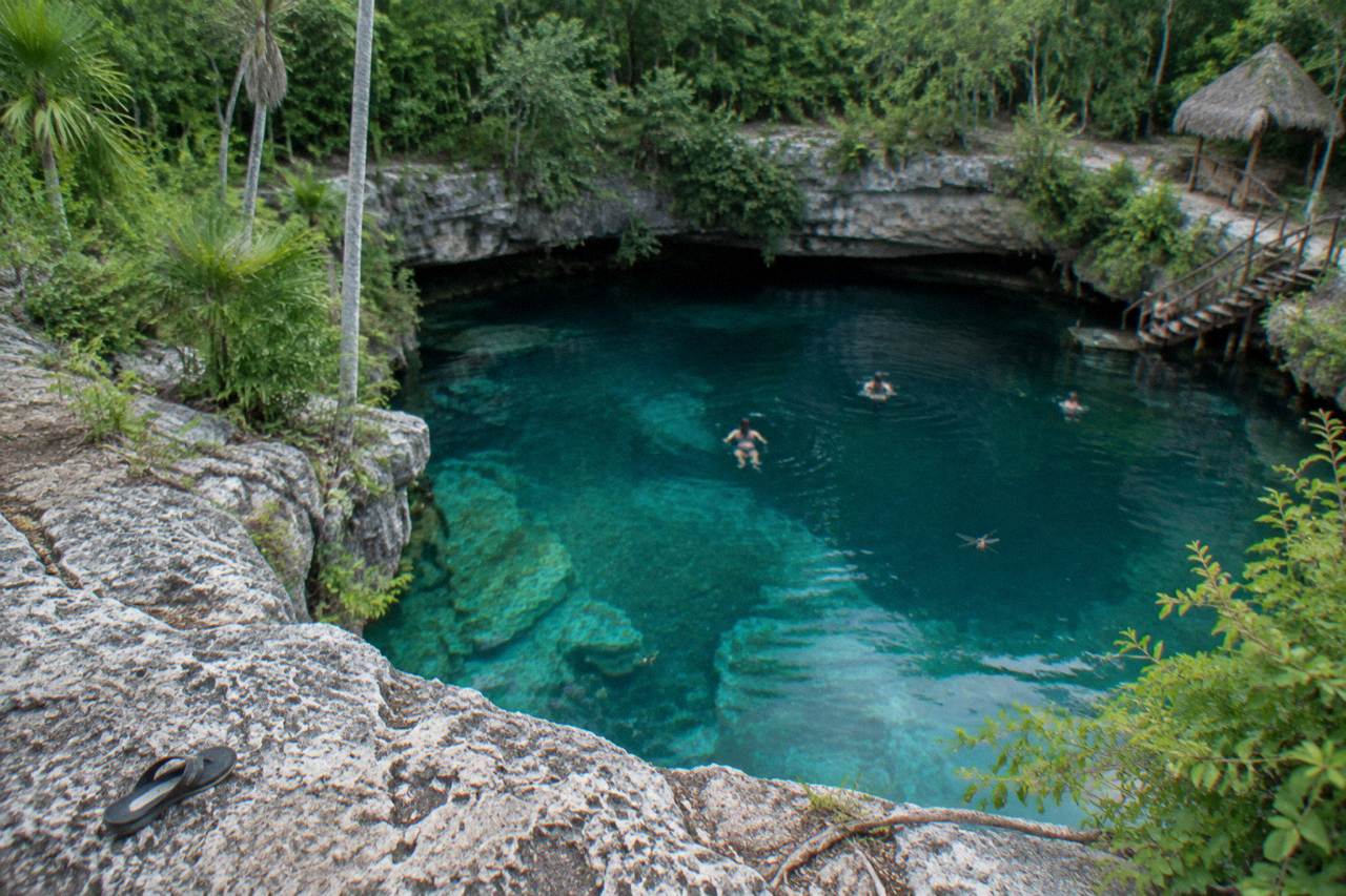 Clear turquoise water in an open cenote surrounded by limestone rock and jungle vegetation