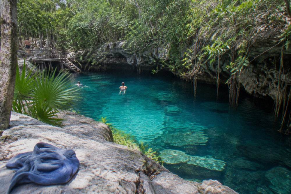 A limestone cenote pool surrounded by jungle foliage and exposed rock