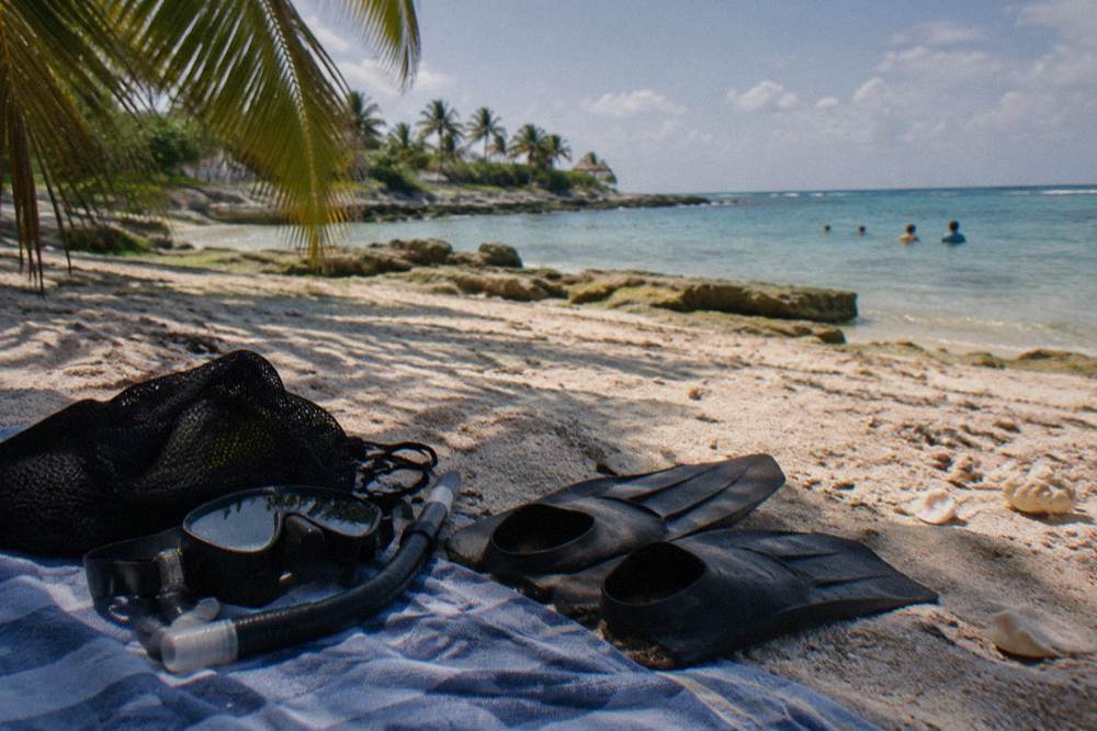 Snorkel mask and fins resting on a beach towel beside shaded sand