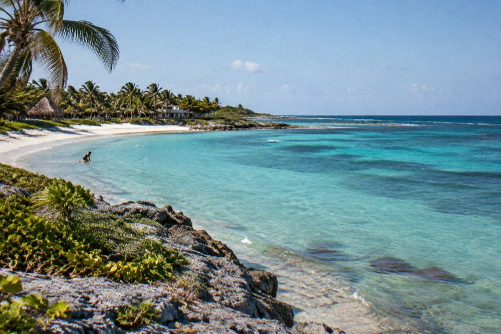Quiet crescent beach with clear shallow water fading to deep blue beyond a reef line