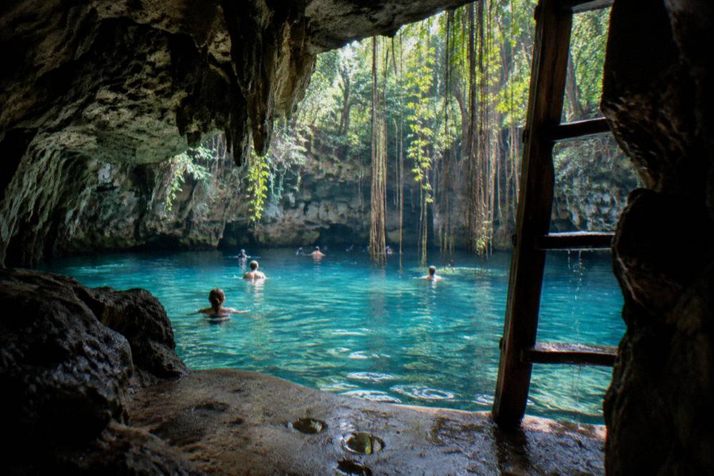 A freshwater sinkhole pool surrounded by rock and jungle vegetation with clear pale blue water