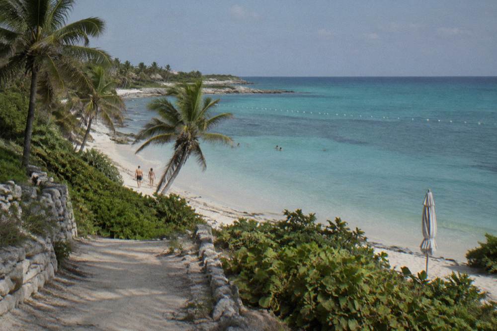 A calm Riviera Maya bay with buoys marking a swimming area and palm trees on the shore