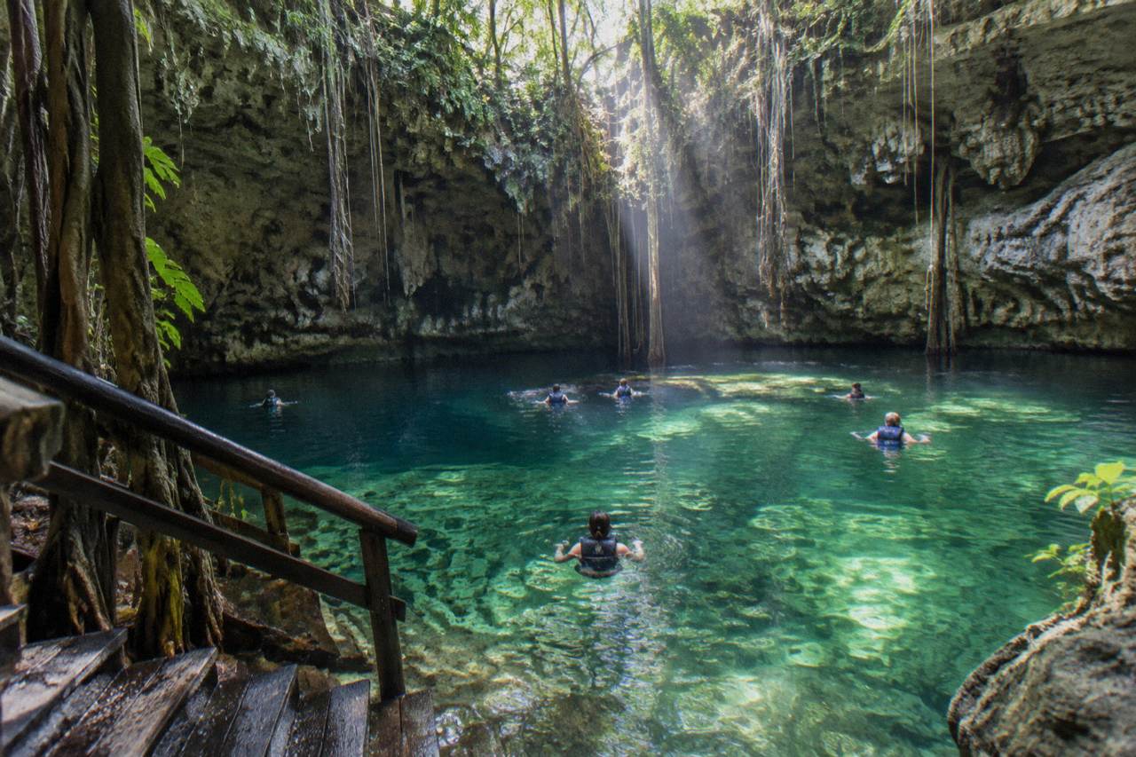 Cenote and Tulum turtle day trips: a clear freshwater cenote pool framed by jungle, with Caribbean bay snorkeling as the second stop